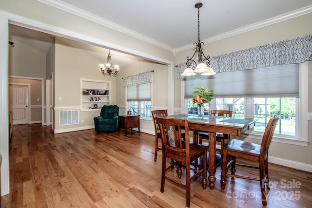 dining area with wood finished floors, a chandelier, built in shelves, visible vents, and crown molding