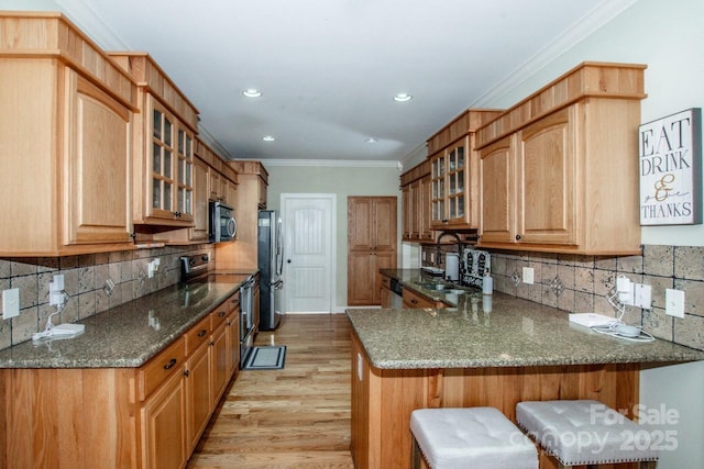 kitchen with light wood-style flooring, glass insert cabinets, a sink, stainless steel appliances, and a kitchen bar