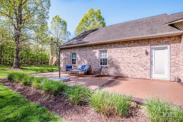 back of property featuring roof with shingles, a yard, a patio area, and brick siding