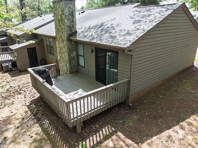 back of property with central air condition unit, a shingled roof, a chimney, a deck, and a storage unit