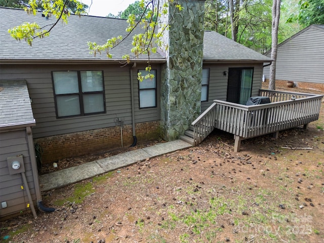 rear view of house featuring a deck, a chimney, and roof with shingles