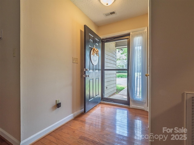 entryway with a textured ceiling, visible vents, hardwood / wood-style floors, and baseboards