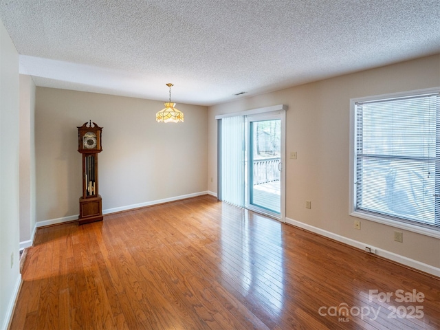 spare room with a textured ceiling, light wood-type flooring, a notable chandelier, and baseboards