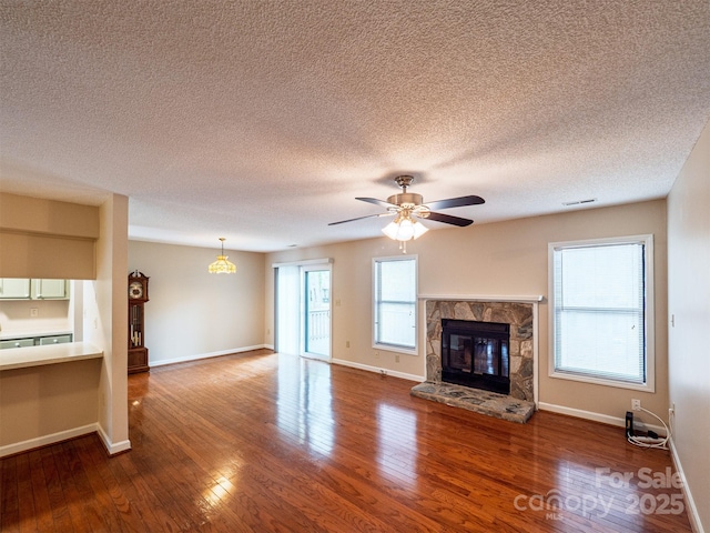 unfurnished living room with a textured ceiling, ceiling fan, baseboards, wood finished floors, and a stone fireplace