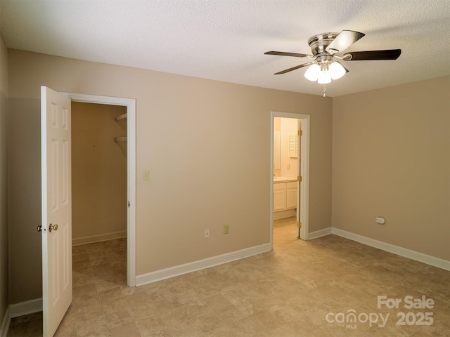 unfurnished bedroom featuring connected bathroom, a closet, a walk in closet, a ceiling fan, and a textured ceiling