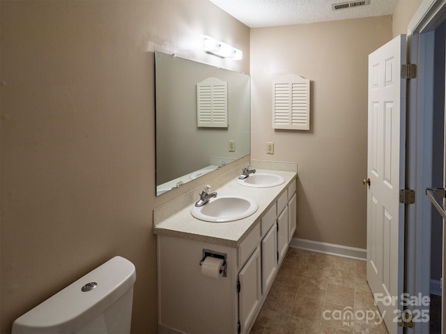 bathroom with toilet, double vanity, a sink, and visible vents