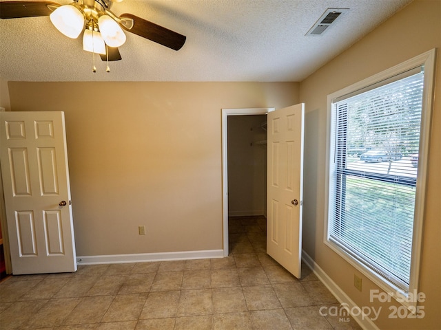 unfurnished bedroom with a textured ceiling, visible vents, a ceiling fan, and a walk in closet