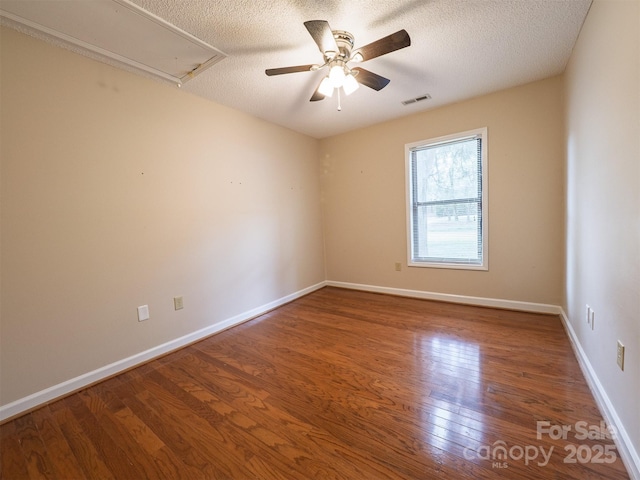 empty room with a textured ceiling, visible vents, ceiling fan, attic access, and wood finished floors