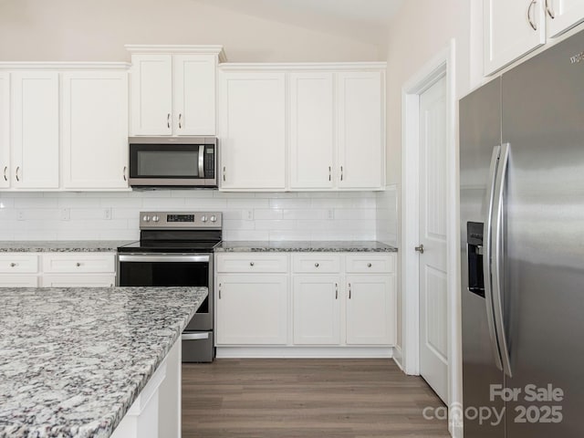 kitchen with dark wood-type flooring, white cabinets, backsplash, vaulted ceiling, and stainless steel appliances