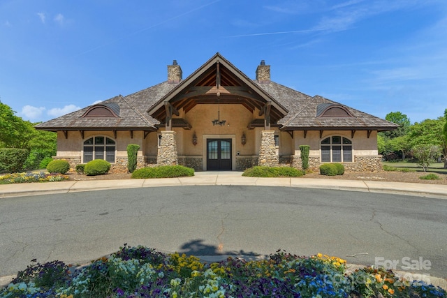 view of front of house featuring stone siding, stucco siding, french doors, and a chimney