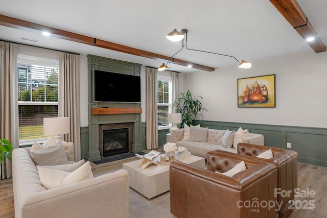 living area with beamed ceiling, light wood finished floors, plenty of natural light, and a fireplace with flush hearth