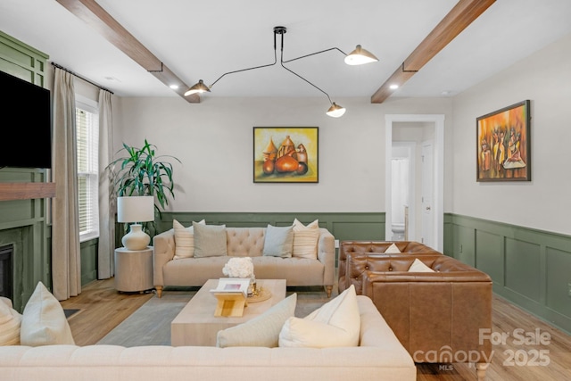 living area with a decorative wall, light wood finished floors, a wainscoted wall, and beam ceiling