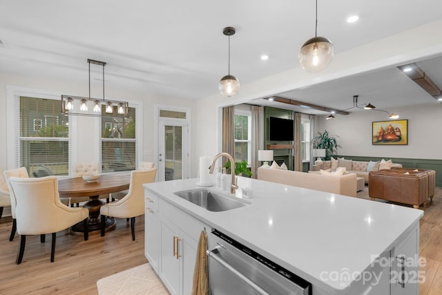 kitchen featuring light wood-style flooring, pendant lighting, stainless steel dishwasher, and a sink