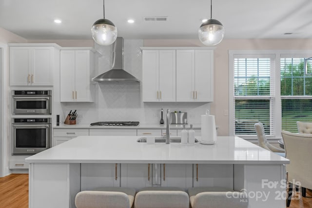 kitchen with a kitchen bar, tasteful backsplash, wall chimney exhaust hood, and hanging light fixtures