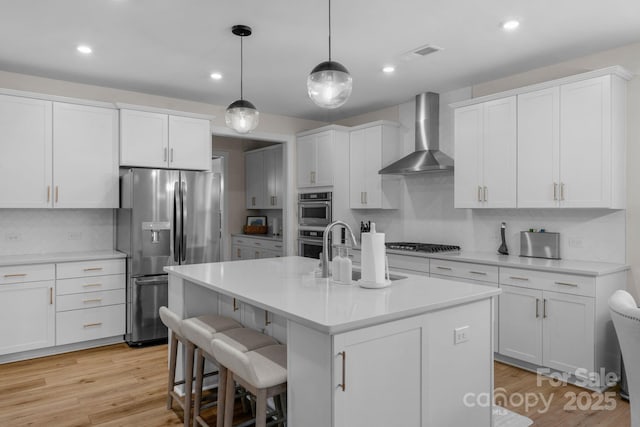 kitchen featuring wall chimney range hood, appliances with stainless steel finishes, a sink, light countertops, and decorative backsplash