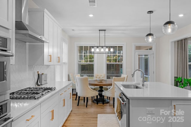 kitchen with visible vents, a sink, wall chimney range hood, light countertops, and appliances with stainless steel finishes