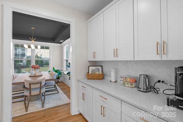 kitchen with white cabinets, backsplash, light countertops, and light wood finished floors