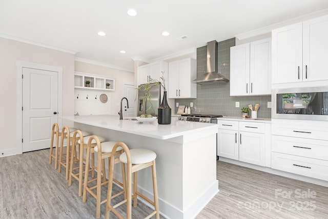 kitchen with ornamental molding, open shelves, a breakfast bar area, wall chimney range hood, and appliances with stainless steel finishes