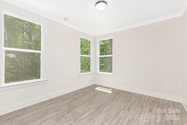 spare room with crown molding, baseboards, visible vents, and wood finished floors