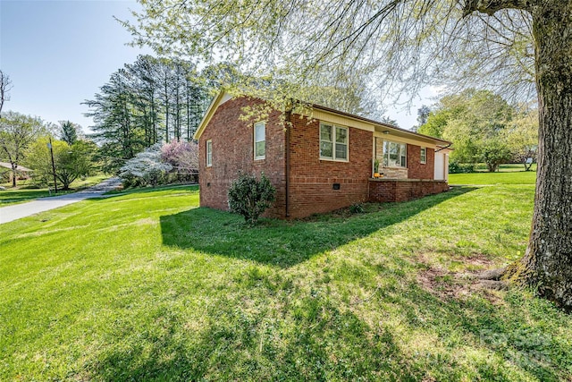 view of side of property featuring crawl space, brick siding, and a lawn
