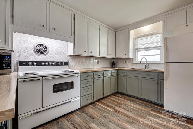 kitchen with white appliances, wood finished floors, a sink, gray cabinetry, and backsplash