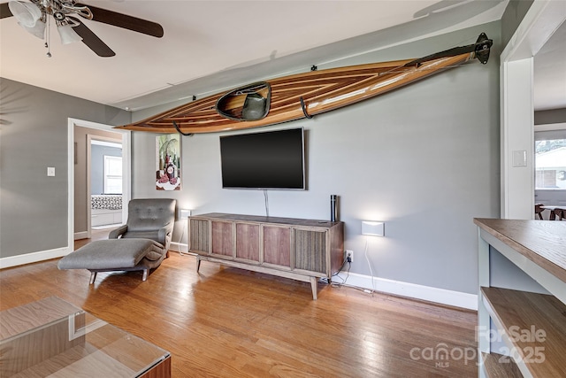 living area with a wealth of natural light, light wood finished floors, baseboards, and a ceiling fan