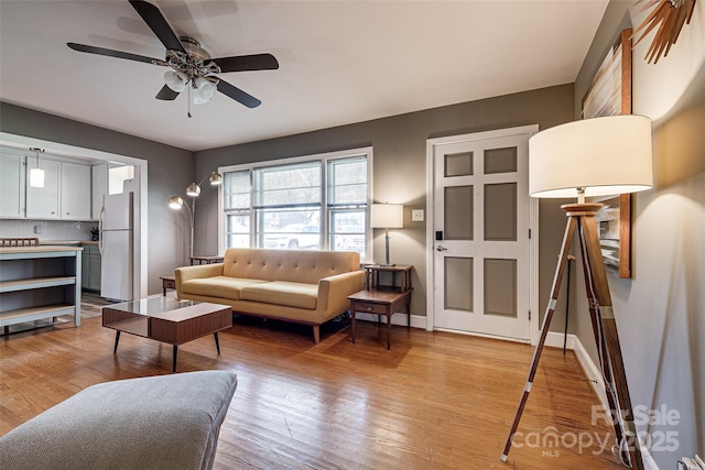 living room featuring ceiling fan, light wood-style floors, and baseboards