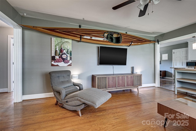 living area featuring wood finished floors, baseboards, and a ceiling fan