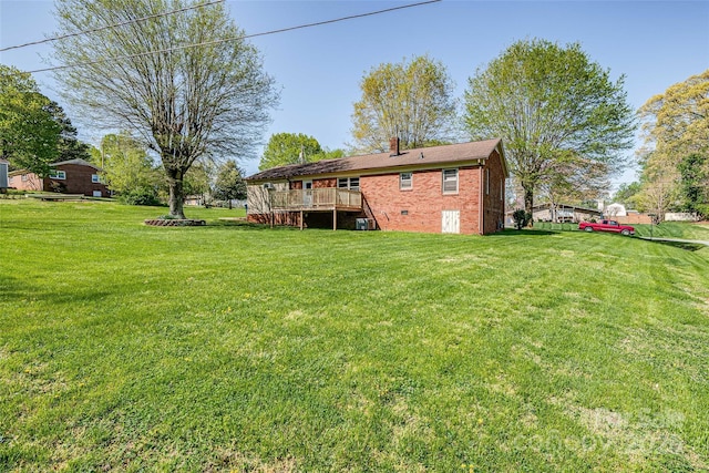 rear view of property with a chimney, brick siding, a wooden deck, and a lawn
