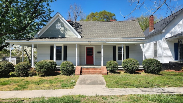 view of front of home with roof with shingles, covered porch, and a front lawn