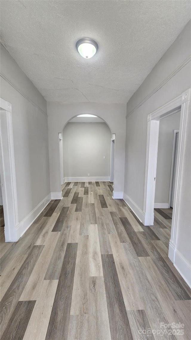 unfurnished room with arched walkways, baseboards, a textured ceiling, and wood finished floors