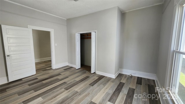 unfurnished bedroom featuring a closet, baseboards, a textured ceiling, and wood finished floors