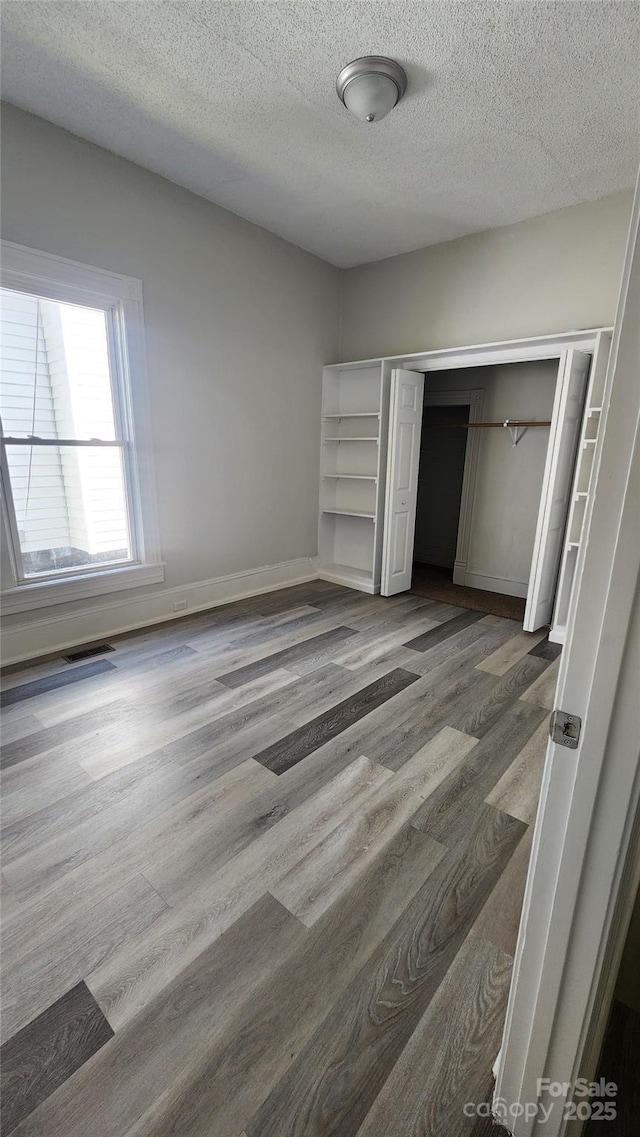 unfurnished bedroom with visible vents, baseboards, a closet, a textured ceiling, and wood finished floors