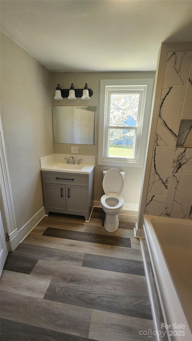 full bath featuring vanity, baseboards, a tub, toilet, and wood finished floors