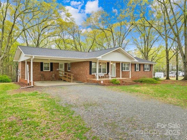 ranch-style house with brick siding, a front yard, a porch, and gravel driveway
