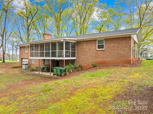 rear view of property with a sunroom, a garage, a chimney, a patio, and brick siding