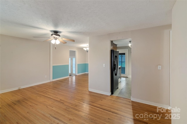 empty room featuring light wood-type flooring, ceiling fan with notable chandelier, baseboards, and a textured ceiling