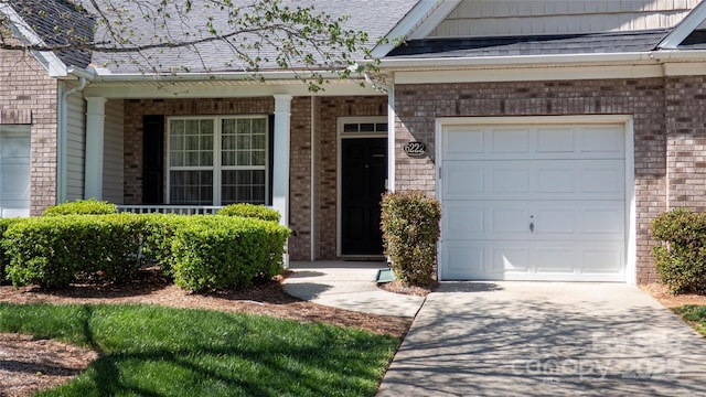 property entrance with roof with shingles, driveway, brick siding, a garage, and covered porch