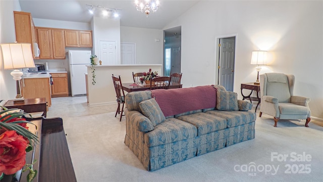 living area featuring high vaulted ceiling, rail lighting, an inviting chandelier, and light carpet