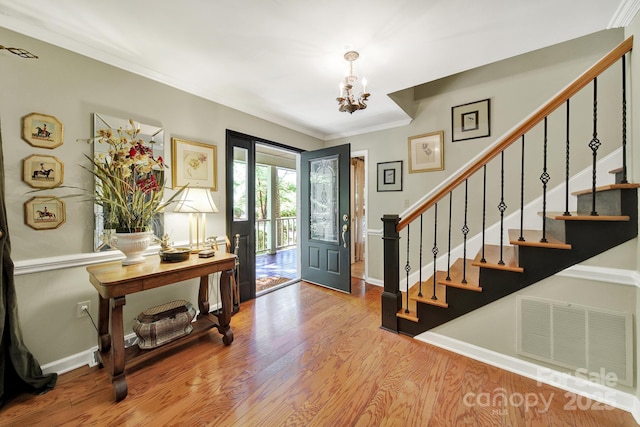 entryway with visible vents, crown molding, wood finished floors, an inviting chandelier, and stairs