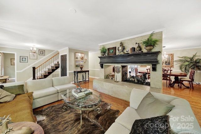 living room featuring wood finished floors, stairway, baseboards, a notable chandelier, and ornamental molding