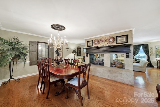 dining room with a multi sided fireplace, crown molding, wood finished floors, baseboards, and an inviting chandelier