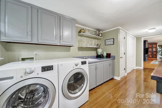 clothes washing area featuring baseboards, washer and clothes dryer, cabinet space, and light wood-style flooring