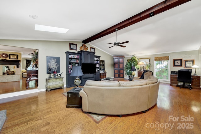 living area featuring a ceiling fan, light wood finished floors, vaulted ceiling with skylight, and ornamental molding