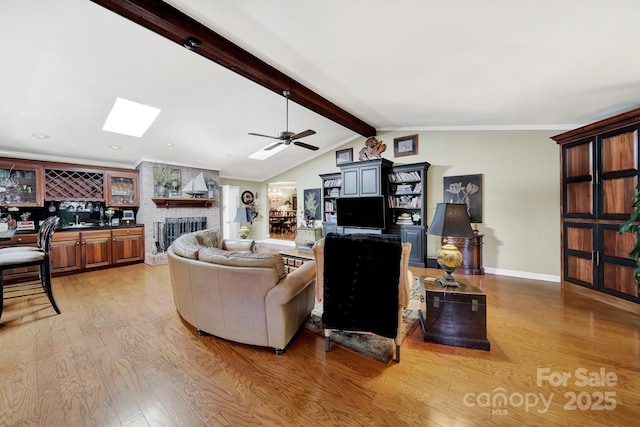 living room featuring light wood-style floors, vaulted ceiling with skylight, a fireplace, and a ceiling fan
