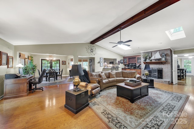living area featuring a brick fireplace, wood finished floors, vaulted ceiling with skylight, and ceiling fan with notable chandelier