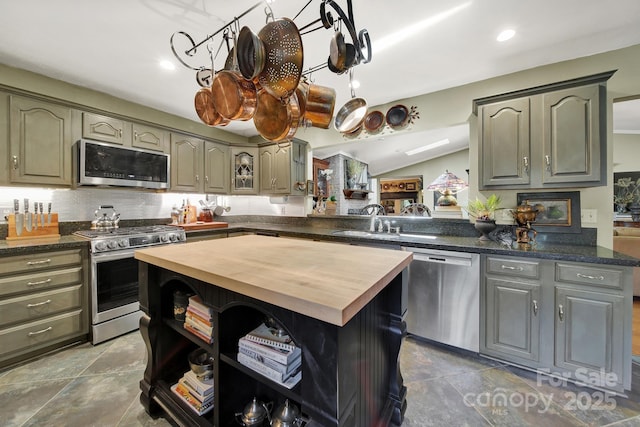 kitchen featuring a kitchen island, wooden counters, a sink, appliances with stainless steel finishes, and vaulted ceiling