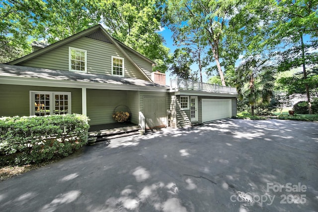 view of property exterior with an attached garage, driveway, a chimney, and roof with shingles
