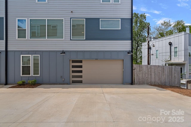exterior space featuring an attached garage, board and batten siding, concrete driveway, and fence