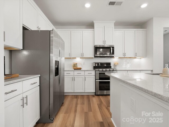 5532 Muckross Ln, Fort Mill, SC 29707 - kitchen featuring tasteful backsplash, visible vents, white cabinets, light wood finished floors, and stainless steel appliances